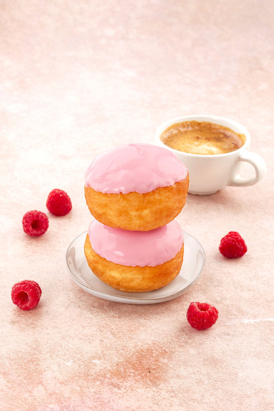 Glutenfria munkar med rosa glasyr och färska hallon serverade med kaffe